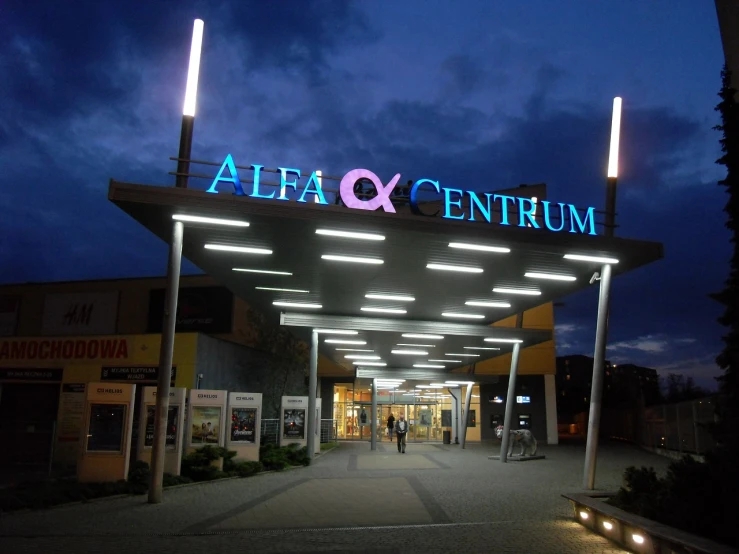 the entrance to a shopping center lit up at night, a picture, by Alfons von Czibulka, stern like athena, outdoor fairgrounds, alpha movie, neofuture