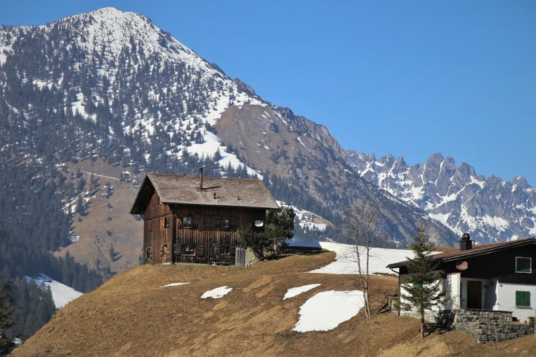 a house on a hill with a mountain in the background, a picture, by Fritz Glarner, pexels, spring winter nature melted snow, chalet, h.r. geiger, base