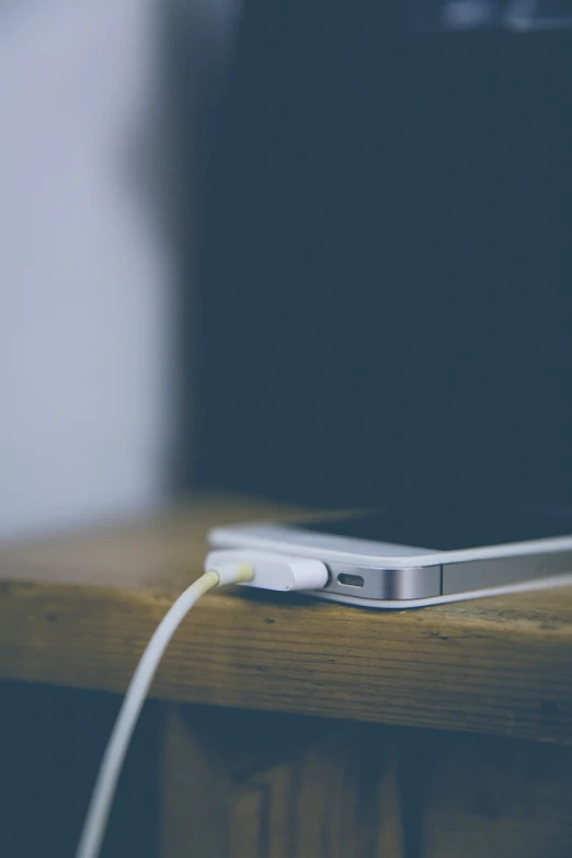 a cell phone sitting on top of a wooden table, by Karl Buesgen, cable plugged in, beautiful iphone wallpaper, vintage color, close-up photo