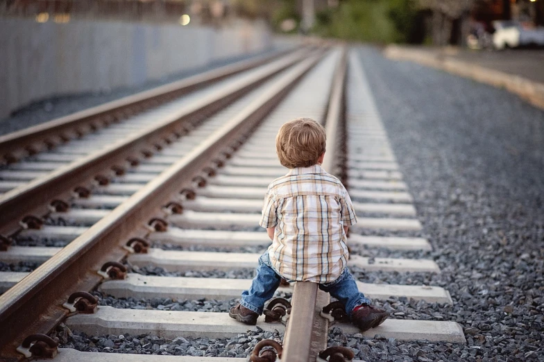 a little boy sitting on a rail road track, unsplash, istockphoto, trainwreck, sittin, hugging his knees