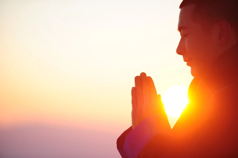 a man is praying with the sun setting in the background, by Jeanna bauck, shutterstock, sukhasana, priest, high details!, sunburst behind woman