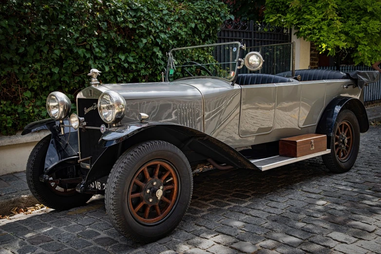 a vintage car parked on a cobblestone street, a portrait, by Carlo Martini, trending on pixabay, art nouveau, grey metal body, 1 9 2 0 s cloth style, vintage - w 1 0 2 4, looking from side!