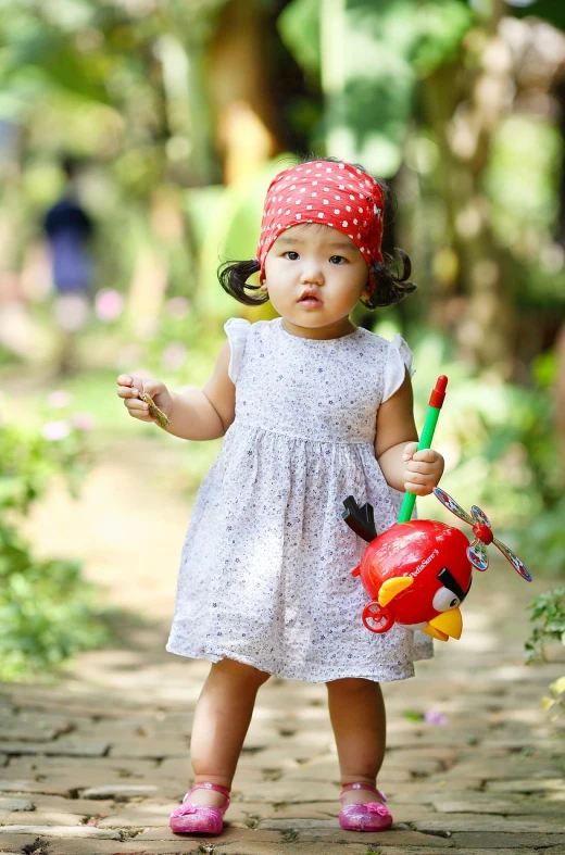 a little girl holding a watering can and a toy, a picture, by Basuki Abdullah, pexels, red bird, holding a spear, square, red headband