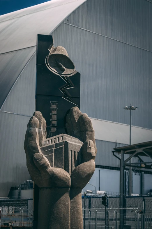 a statue of a hand holding a clock in front of a building, an abstract sculpture, nuclear art, stood in a factory, taken with sony alpha 9, in style of zaha hadid architect, reactor