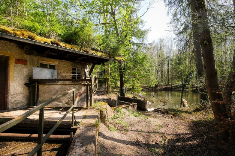 a cabin in the woods next to a body of water, by Karl Hagedorn, les nabis, a ghetto in germany, water wheel, realistic wide angle photo, nice spring afternoon lighting