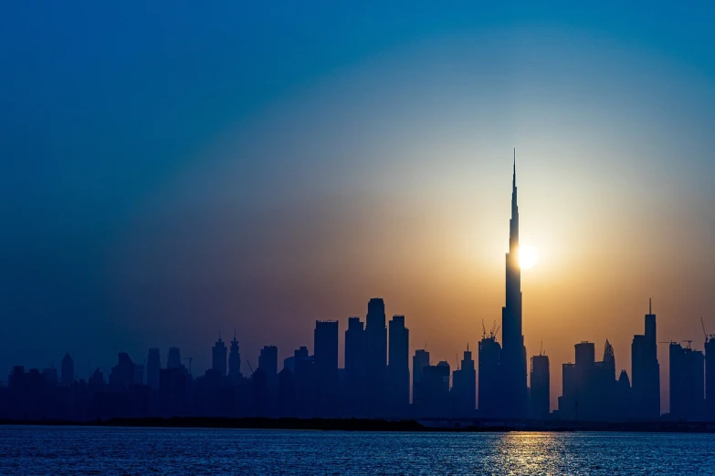 a large body of water with a city in the background, a picture, by Tom Wänerstrand, pexels contest winner, dubai, sun shafts, silhouetted, istockphoto