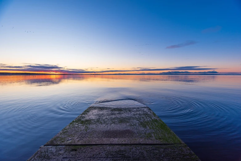 a dock in the middle of a body of water, a picture, by Holger Roed, shutterstock, blue sky at sunset, ripples, color ( sony a 7 r iv, road to the sea