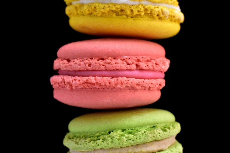a stack of macarons sitting on top of each other, inspired by François Louis Thomas Francia, pop art, against a deep black background, detailed zoom photo, trio, sherbert sky