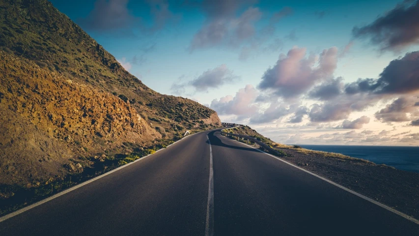 a car that is sitting on the side of a road, by Alexis Grimou, shutterstock, minimalism, wide angle landscape photography, going forward to the sunset, the mountain is steep, coastal