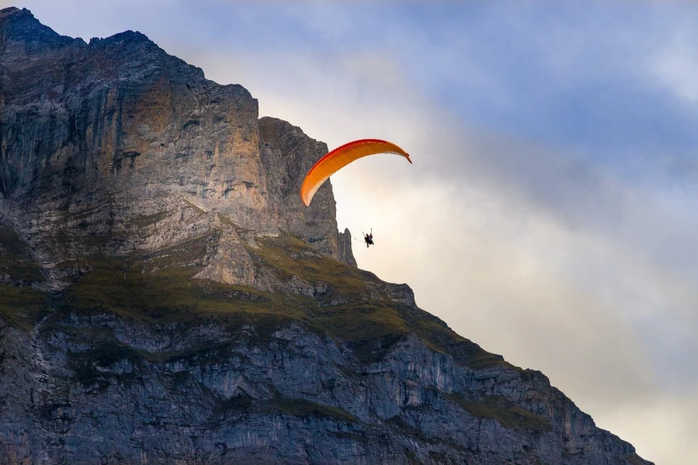 a person flying a kite on top of a mountain, a picture, by Cedric Peyravernay, shutterstock, lauterbrunnen valley, parachutes, in the evening, panning shot