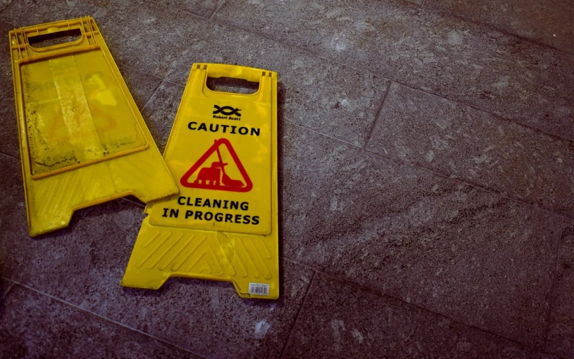 a caution sign sitting on the ground next to a wet floor, by Niko Henrichon, pexels, happening, 🦩🪐🐞👩🏻🦳, yellow robes, cleaning future, taken in the late 2000s