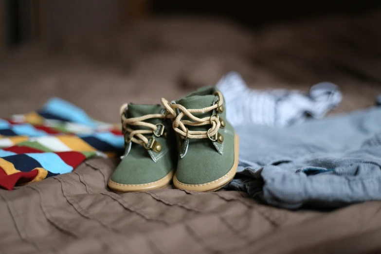 a pair of green shoes sitting on top of a bed, pexels, green and brown clothes, toddler, militaristic, cloth accessories