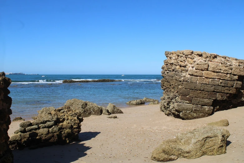 a couple of large rocks sitting on top of a sandy beach, a portrait, epic vista of old ruins, on the beach at noonday, victorian arcs of sand, wall