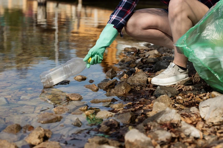 a woman picking up a plastic bottle from a river, a picture, shutterstock, marine microbiology, using a spade, closeup photo, professional photo