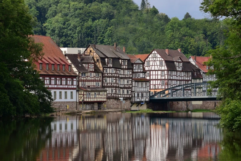 a large body of water with a bridge over it, heidelberg school, timbered house with bricks, white buildings with red roofs, log houses built on hills, reflecting