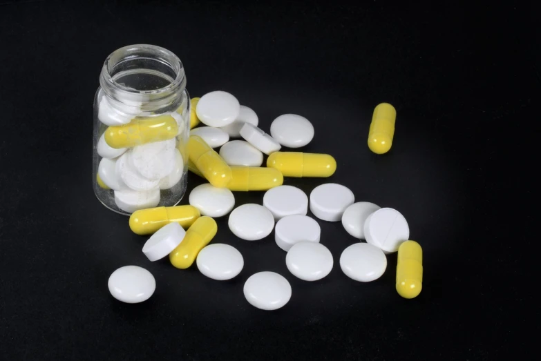 a glass jar filled with white and yellow pills, antipodeans, on black background, 33mm photo