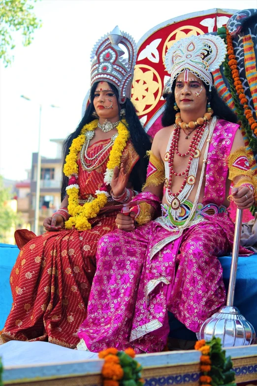 a couple of people sitting on top of a float, samikshavad, dressed as an oracle, beautiful faces, transgender, walking