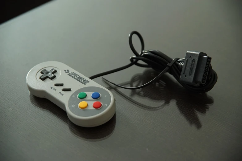 a video game controller sitting on top of a table, by Hiroyuki Tajima, unsplash, neogeo, cable plugged in, on grey background, colorful and grayish palette, close up angle