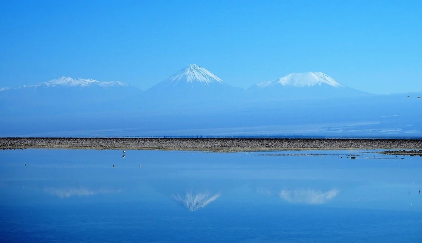 a body of water with mountains in the background, a photo, by Andrei Kolkoutine, flickr, mingei, reflecting mount fuji, ivan bolivian, cranes, blue sand