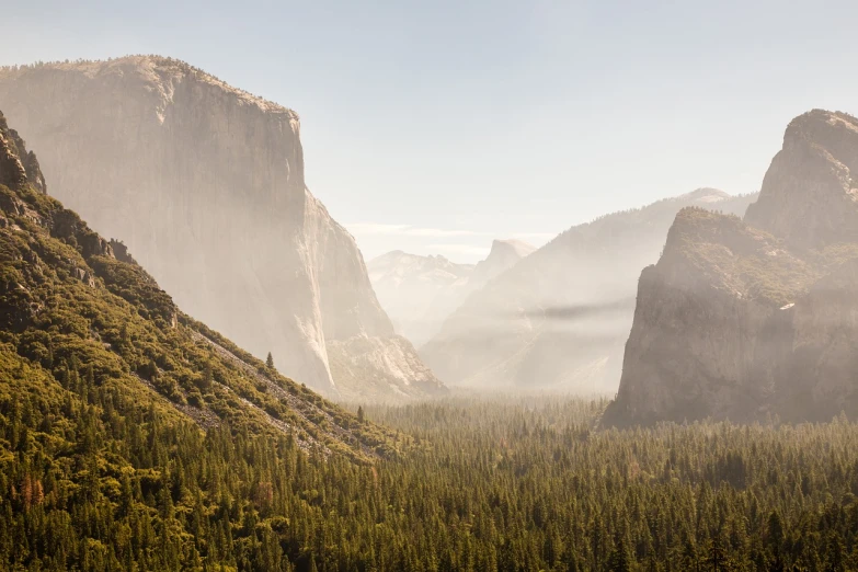 a view of a valley with mountains in the background, by Andrew Domachowski, shutterstock, visual art, yosemite valley, light mist, dissolving into the air, wide angle landscape photography