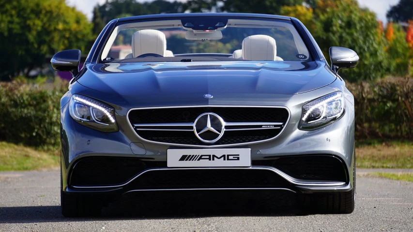 a silver car driving down a road with trees in the background, trending on pixabay, modernism, mercedez benz, convertible, front of car angle, transparent black windshield