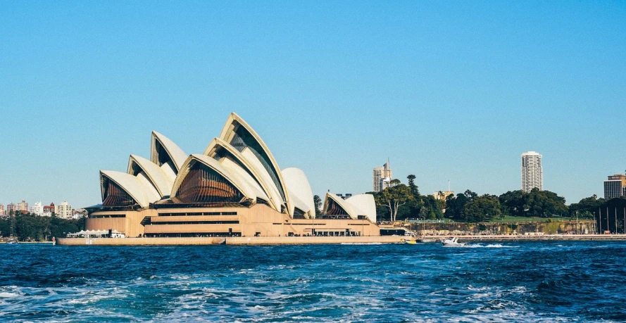 a large building sitting on top of a body of water, inspired by Sydney Carline, trending on unsplash, modernism, with great domes and arches, coast as the background, mobile wallpaper, sails