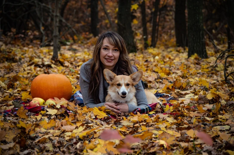 a woman laying in the leaves with a dog, a portrait, by Maksimilijan Vanka, corgi, pumpkin patch, 1 3 5 mm nikon portrait, family photo