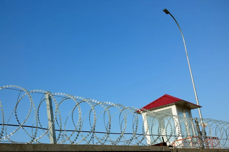 a red roof sitting on top of a building next to a barbed wire fence, a portrait, by Hristofor Zhefarovich, shutterstock, blue wall, military base, circular gate in a white wall, modern high sharpness photo