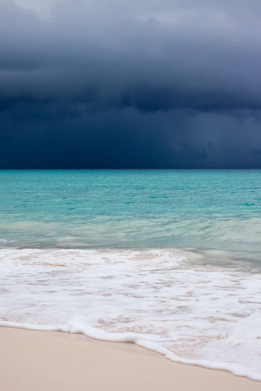 a large body of water sitting on top of a sandy beach, a photo, by Alexander Scott, stormy lighting, bahamas, blue and black, rain