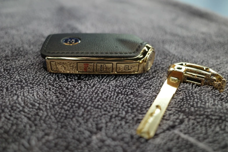 a cell phone sitting on top of a towel next to a key, by Aleksander Kotsis, auto-destructive art, jewelry engraved in scarab, gold trim, very sharp and detailed photo, switch