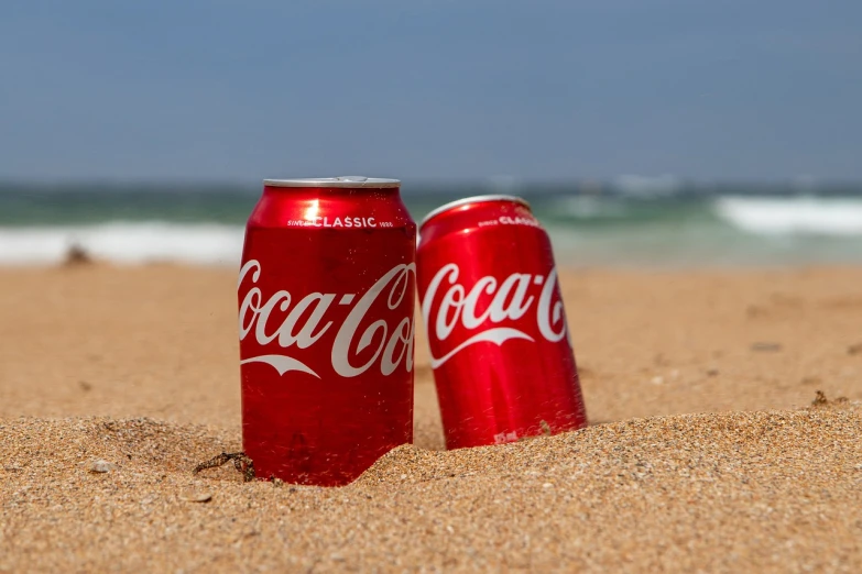 a couple of coke cans sitting on top of a sandy beach, press release, sun coast, octa 8k, tourism