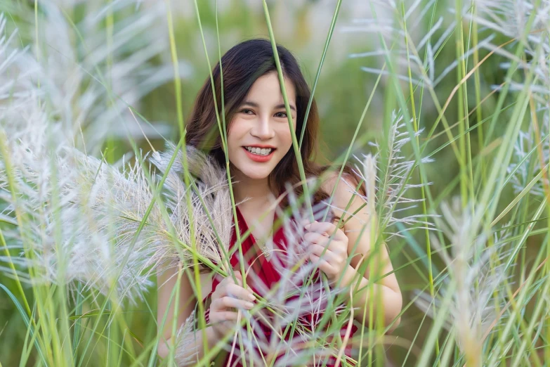 a woman standing in a field of tall grass, a picture, inspired by Kim Du-ryang, pixabay contest winner, cheeky smile with red lips, shot with canon eoa 6 d mark ii, beautiful young asian woman, hiding in grass