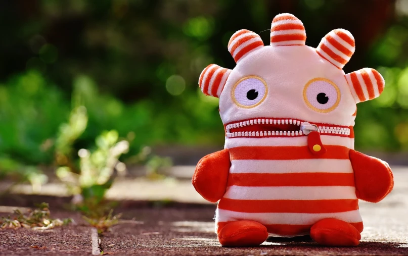 a close up of a stuffed animal on a sidewalk, inspired by Wilson Irvine, pixabay contest winner, red and white stripes, cute monster character design, zippers, desktop wallpaper