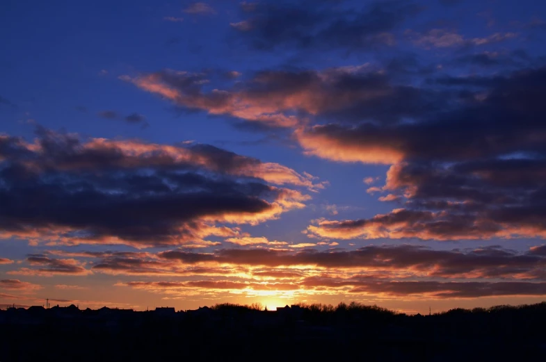 a silhouette of a person flying a kite at sunset, a picture, flickr, romanticism, layered stratocumulus clouds, vista of a city at sunset, orange and blue sky, spring evening