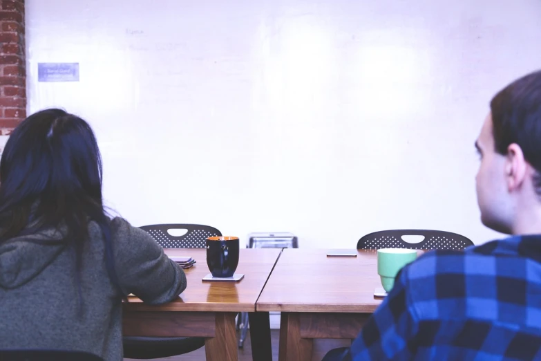 two people sitting at a table in front of a whiteboard, pexels, realism, minimalist environment, grainy photo, next to a cup, backrooms office space
