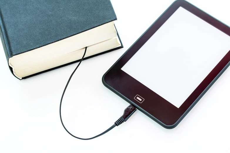 a tablet computer sitting next to a book, cable plugged in, istockphoto, evenly lit, on white paper