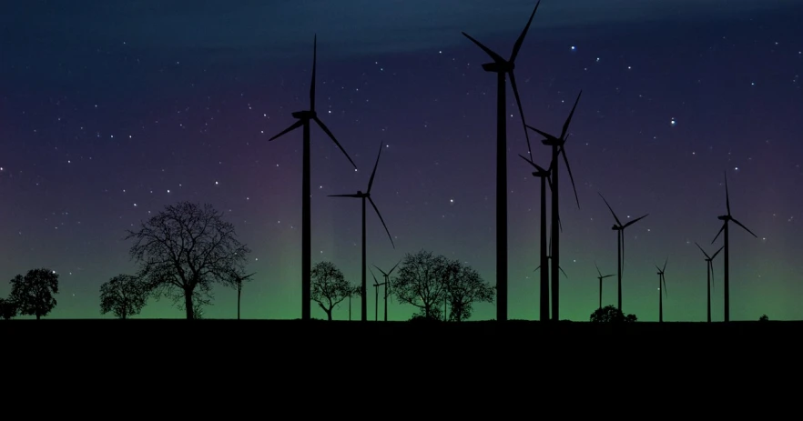 a group of wind turbines sitting on top of a field, a colorized photo, by Jesper Knudsen, northern lights in space, silhouettes, 4k high res, yorkshire