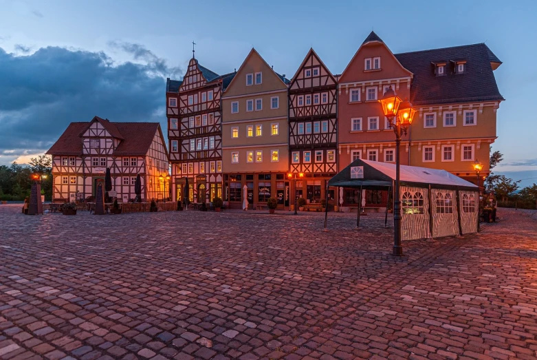 a group of buildings sitting on top of a cobblestone street, by Karl Hagedorn, shutterstock, 8k hdr dusk light, timbered house with bricks, square, lower saxony