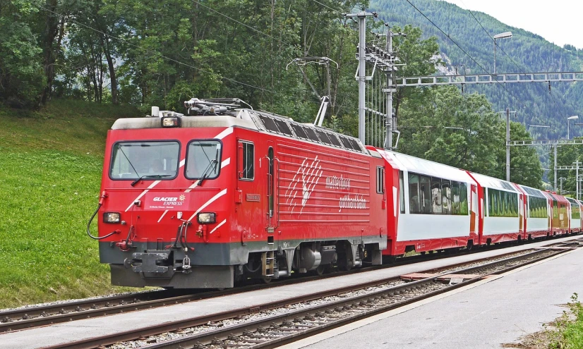 a red train traveling down train tracks next to a lush green hillside, by Ladrönn, flickr, swiss modernizm, electric, 64x64, 800t