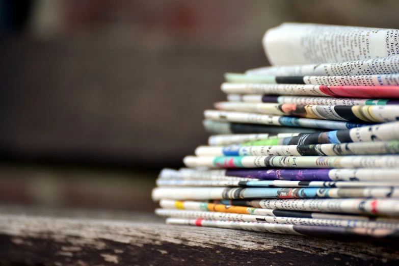 a stack of newspapers sitting on top of a wooden bench, private press, coloured, focusing, facebook post, traditional medium