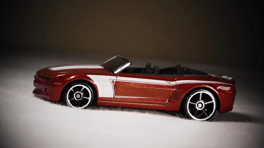 a red toy car sitting on top of a snow covered ground, a tilt shift photo, inspired by Otto Eckmann, mustang, red and white stripes, convertible, maroon metallic accents