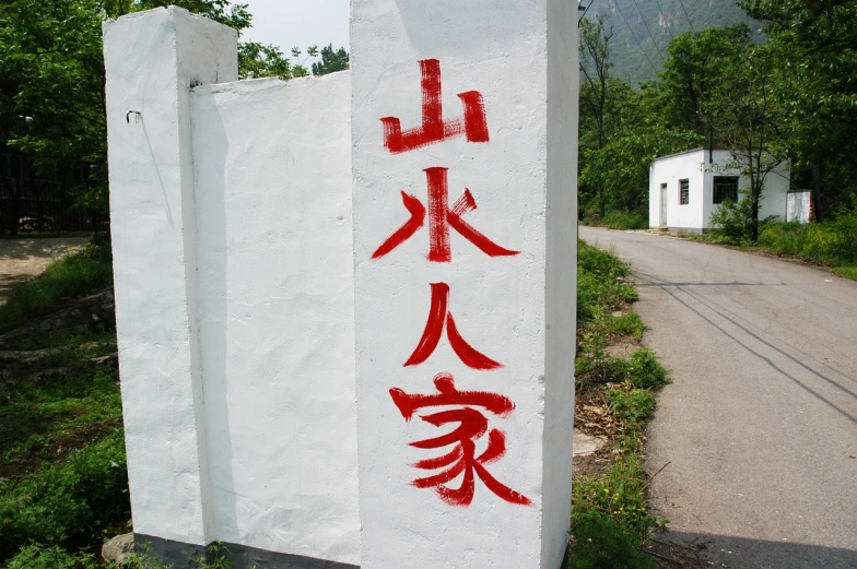 a white sign sitting on the side of a road, a silk screen, inspired by Zhang Zongcang, temporary art, red ink, village, forbidding spirit!!, okami