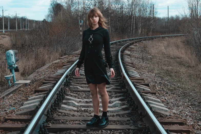 a woman in a black dress standing on a train track, a portrait, inspired by Elsa Bleda, unsplash, surrealism, orthodox symbolism diesel punk, portrait of a young witch girl, she wears boots, girl with warship parts