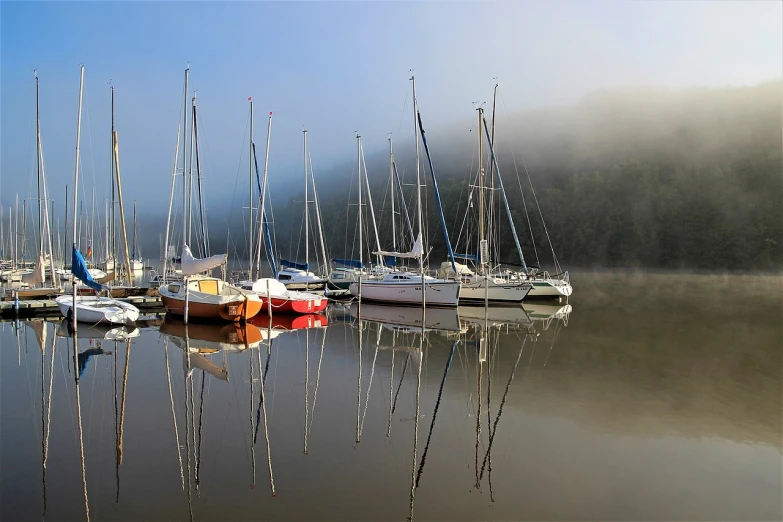 a group of boats sitting on top of a body of water, a photo, by Gerard Soest, pixabay, light morning fog, glossy reflections, sailboat, marsden