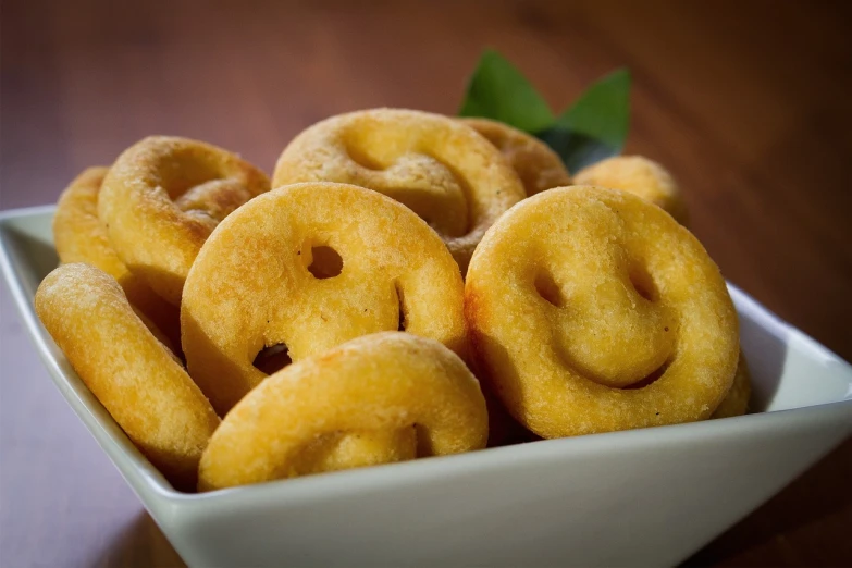 a white bowl filled with doughnuts on top of a wooden table, a portrait, inspired by Chippy, flickr, smiley face, body made out of macaroni, focus on smile, condorito