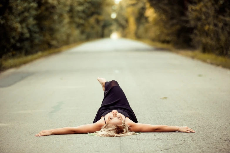 a woman laying on the ground in the middle of a road, a portrait, unsplash, realism, arms open, blonde, in harmony with nature, post-processed