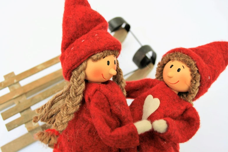 a couple of dolls sitting on top of a wooden bench, by Marie Angel, wearing a red outfit, winter season, heart, elves