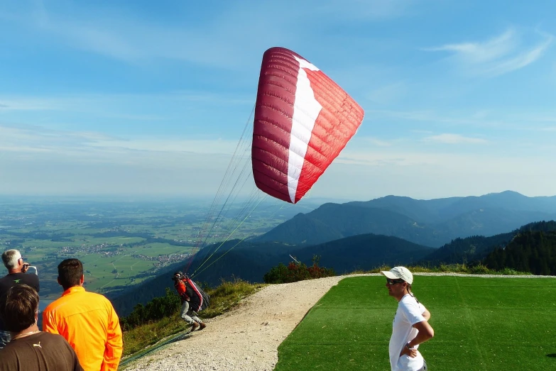 a group of people standing on top of a lush green hillside, by Erwin Bowien, flickr, aerodynamic, air is being pushed around him, with mountains in the background, practice