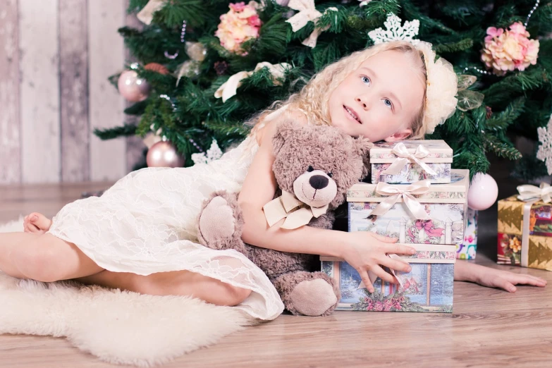 a little girl holding a teddy bear in front of a christmas tree, a photo, by Maksimilijan Vanka, shutterstock, beautiful blonde girl, gifts, lovely bohemian princess, alternate angle