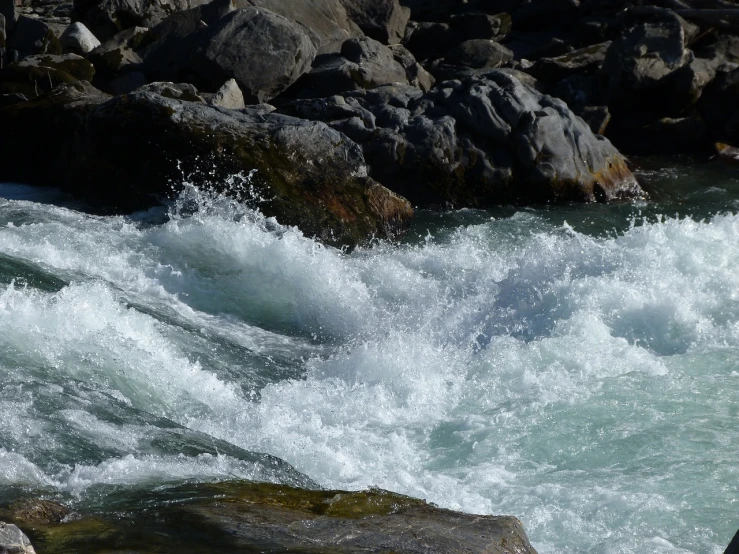 a man riding a wave on top of a surfboard, a picture, hurufiyya, sparkling in the flowing creek, rocks, closeup photo, uttarakhand